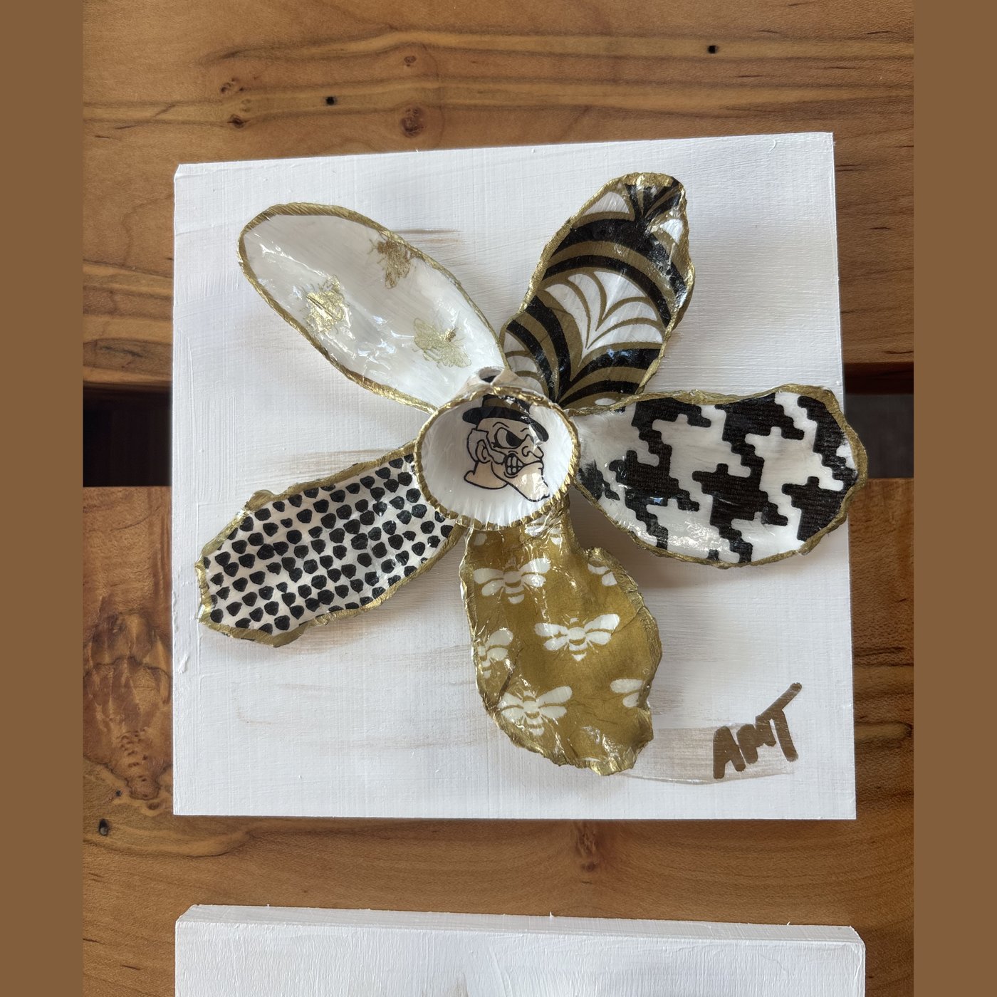 A six-petal shell flower wall art in a black, white, and gold palette with lace, houndstooth, and floral patterns.