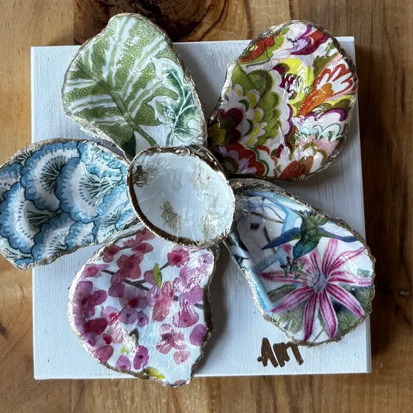 A six-petal shell flower wall art with cherry blossom, hummingbird, and leaf patterns around a gold bee center.