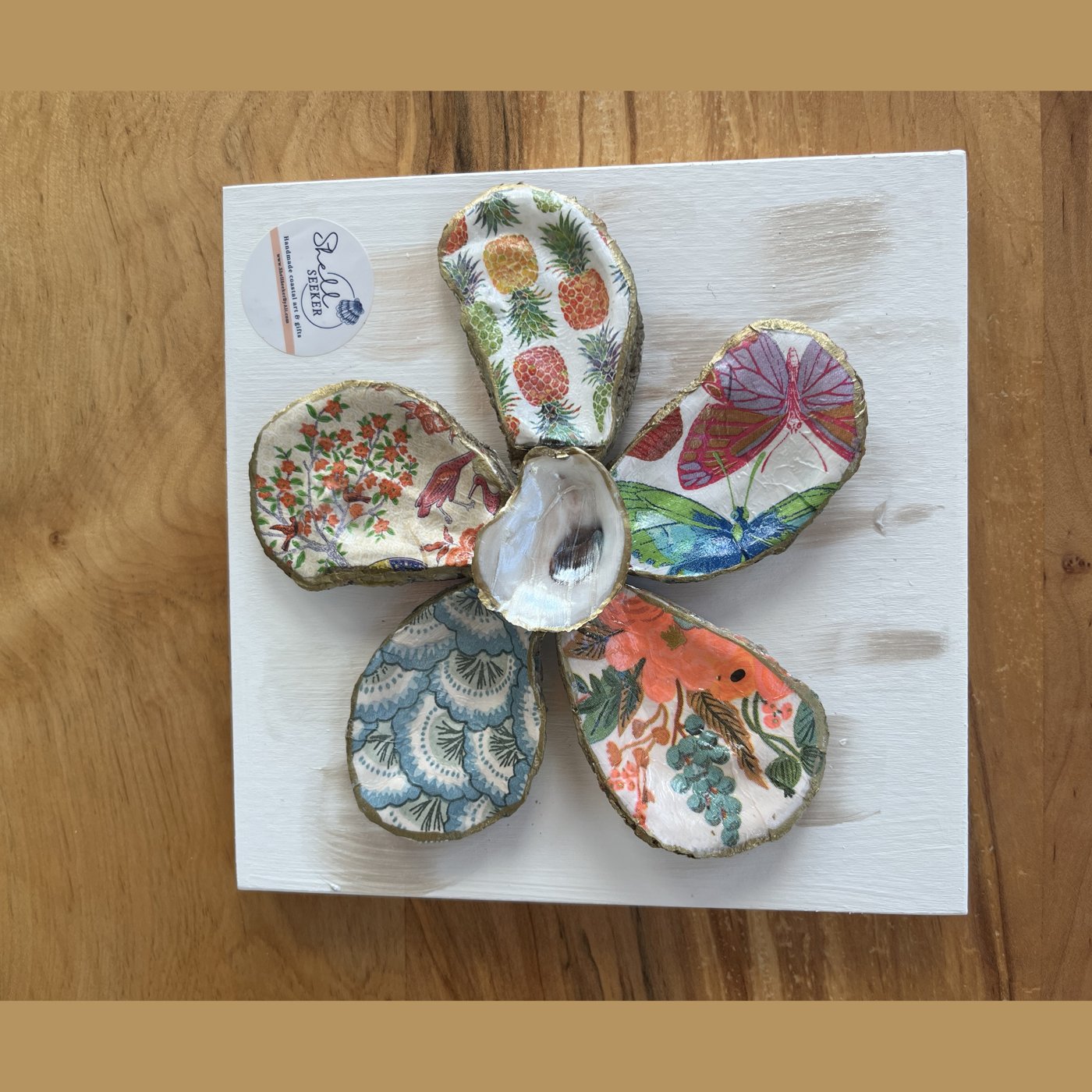 A six-petal shell flower wall art with pineapple, butterfly, and floral patterns around a pearl center.