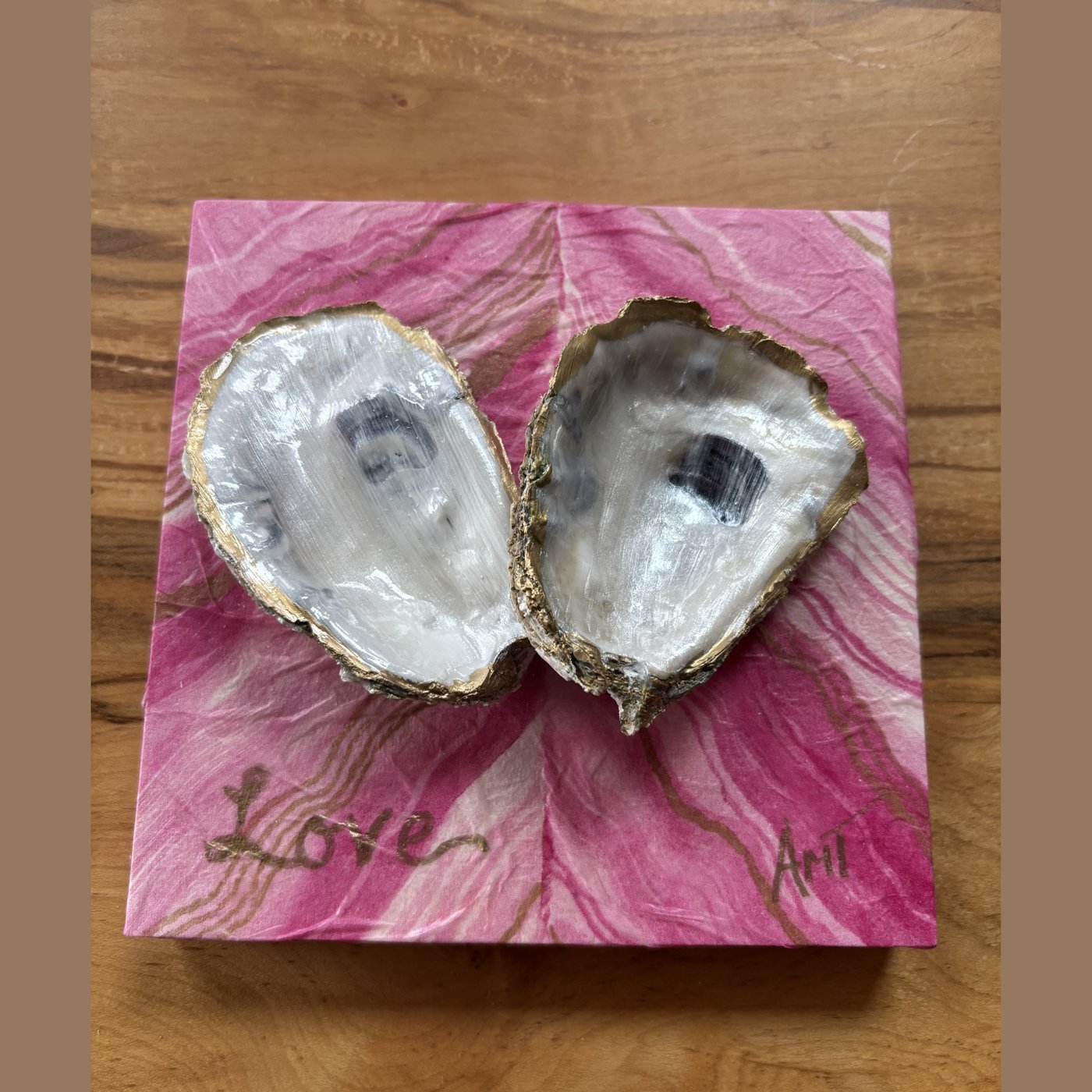 Two natural pearl oyster shells forming a heart on a pink marbled background, hand-lettered "Love."