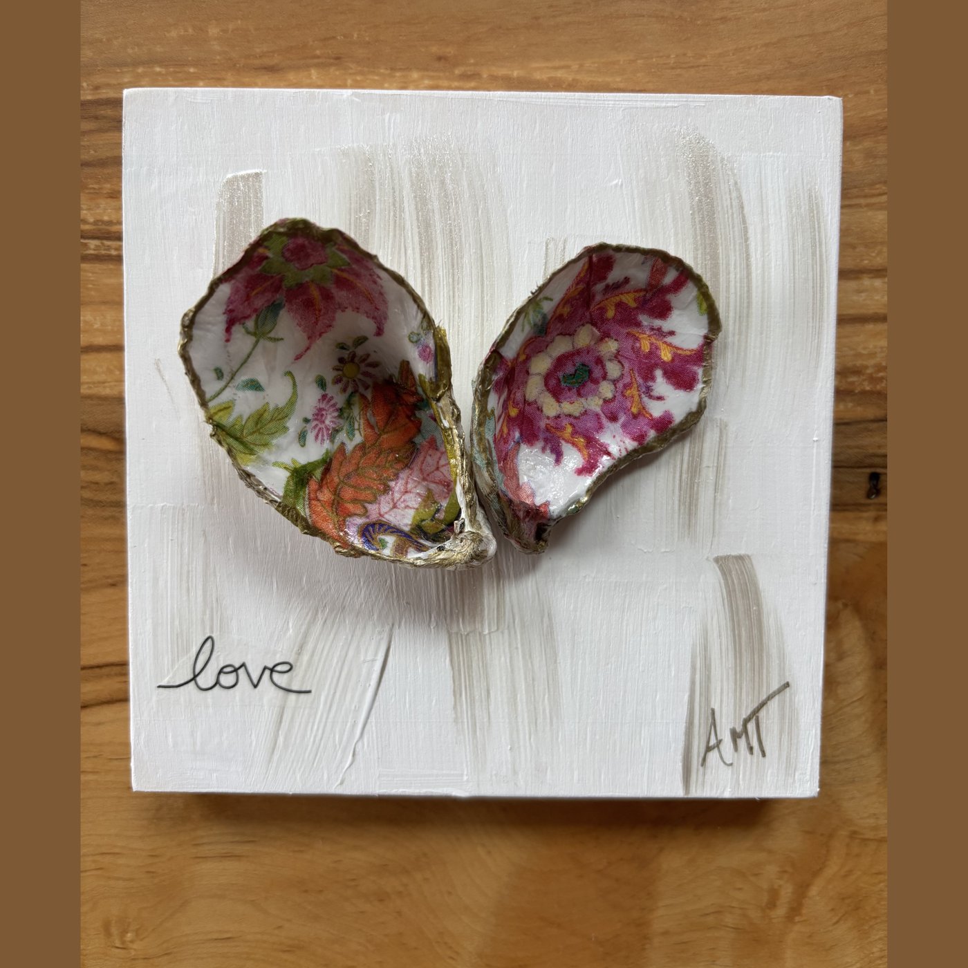 Two oyster shells forming a heart, decorated in a pink and green tobacco leaf floral pattern and hand-lettered "love."