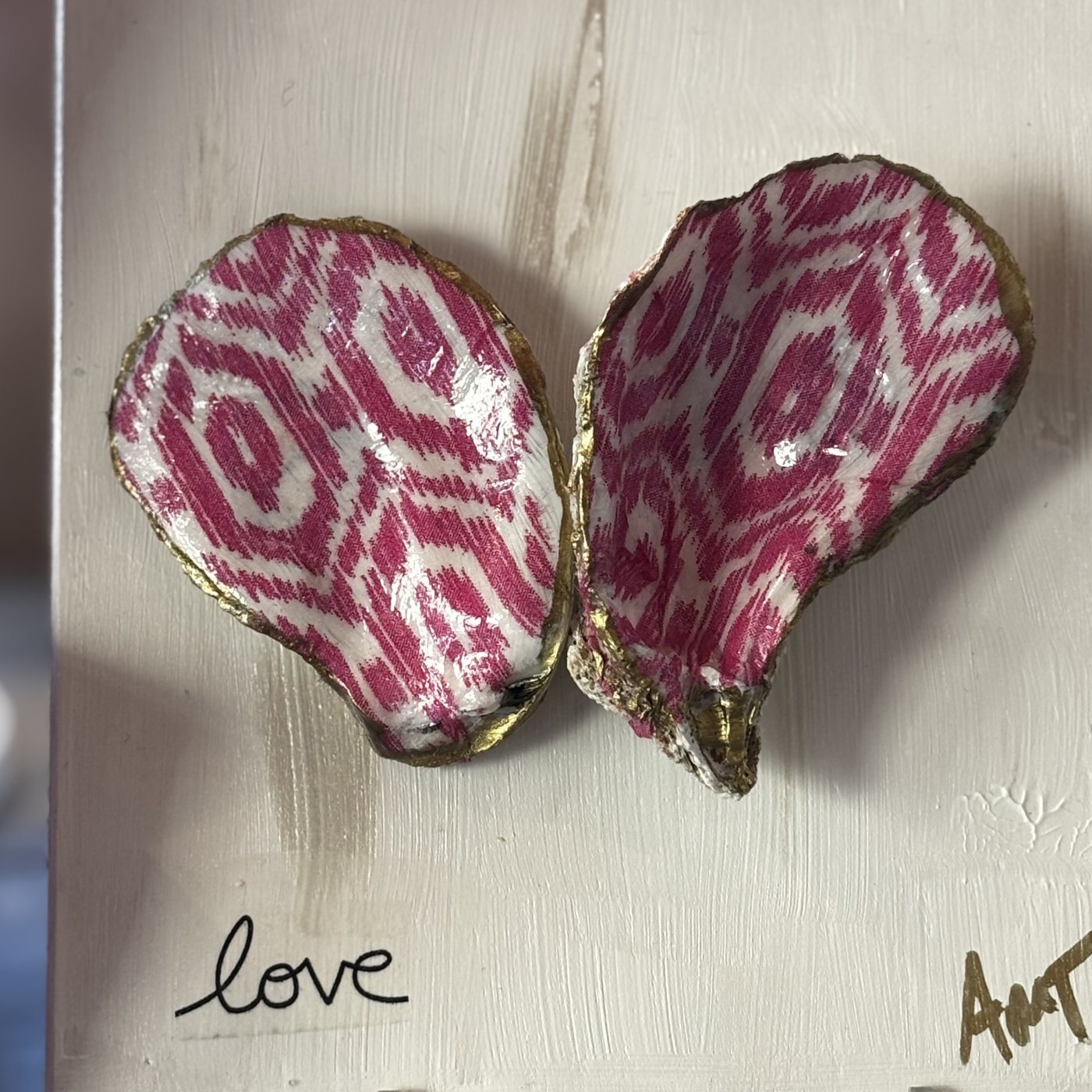 Two oyster shells forming a heart in a pink ikat pattern, hand-lettered "love."