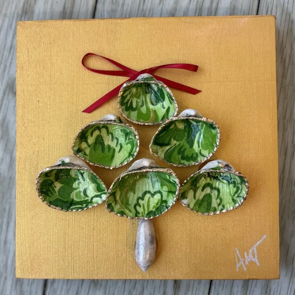 A gold canvas panel with green patterned clam shells arranged into a Christmas tree, topped with a red bow.