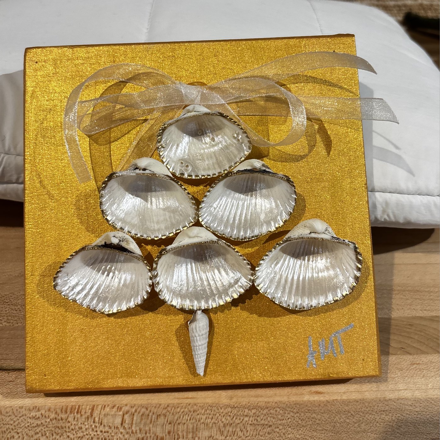 A gold canvas panel with silver scallop shells arranged into a Christmas tree.