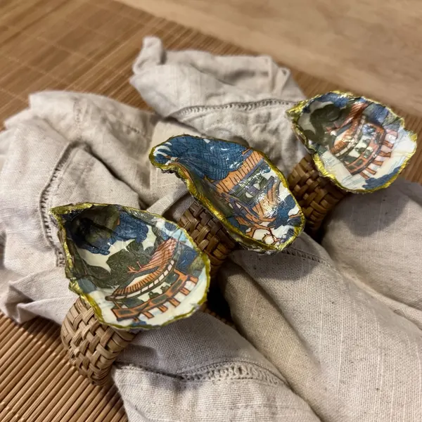 Gold-rimmed oyster shell napkin rings with a blue and orange chinoiserie pagoda scene.