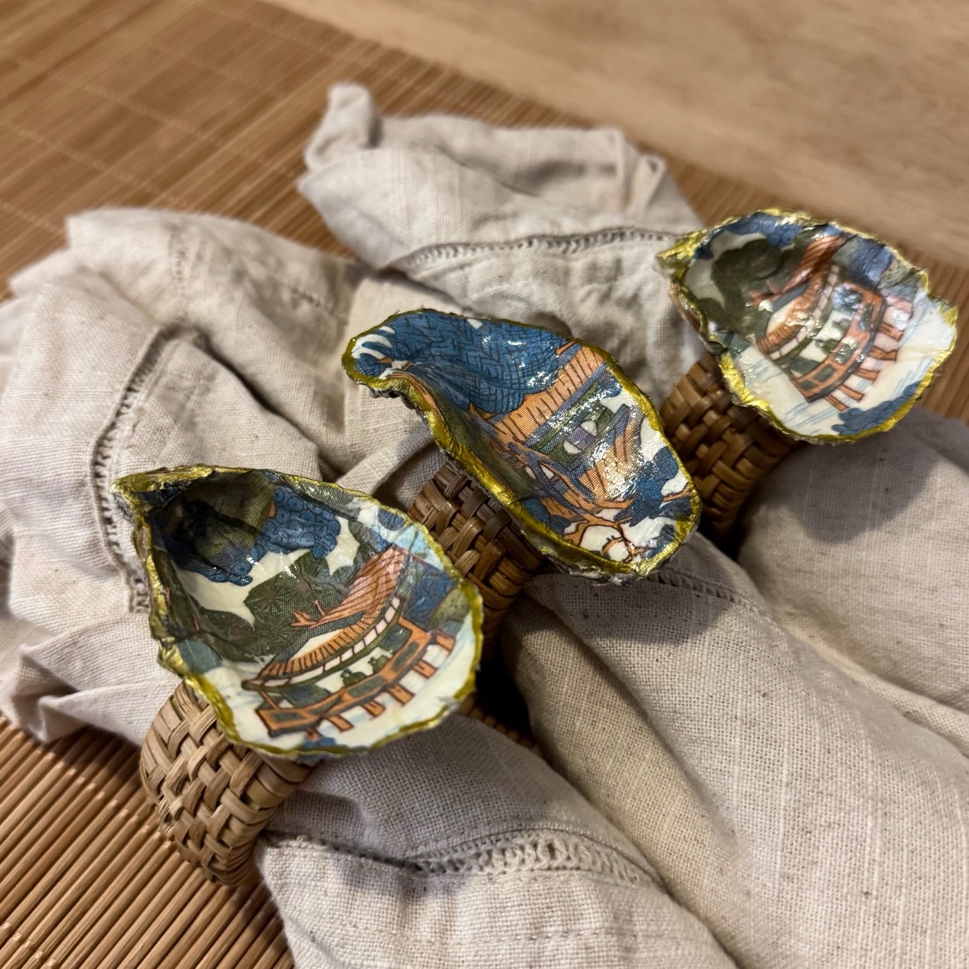 Gold-rimmed oyster shell napkin rings with a blue and orange chinoiserie pagoda scene.