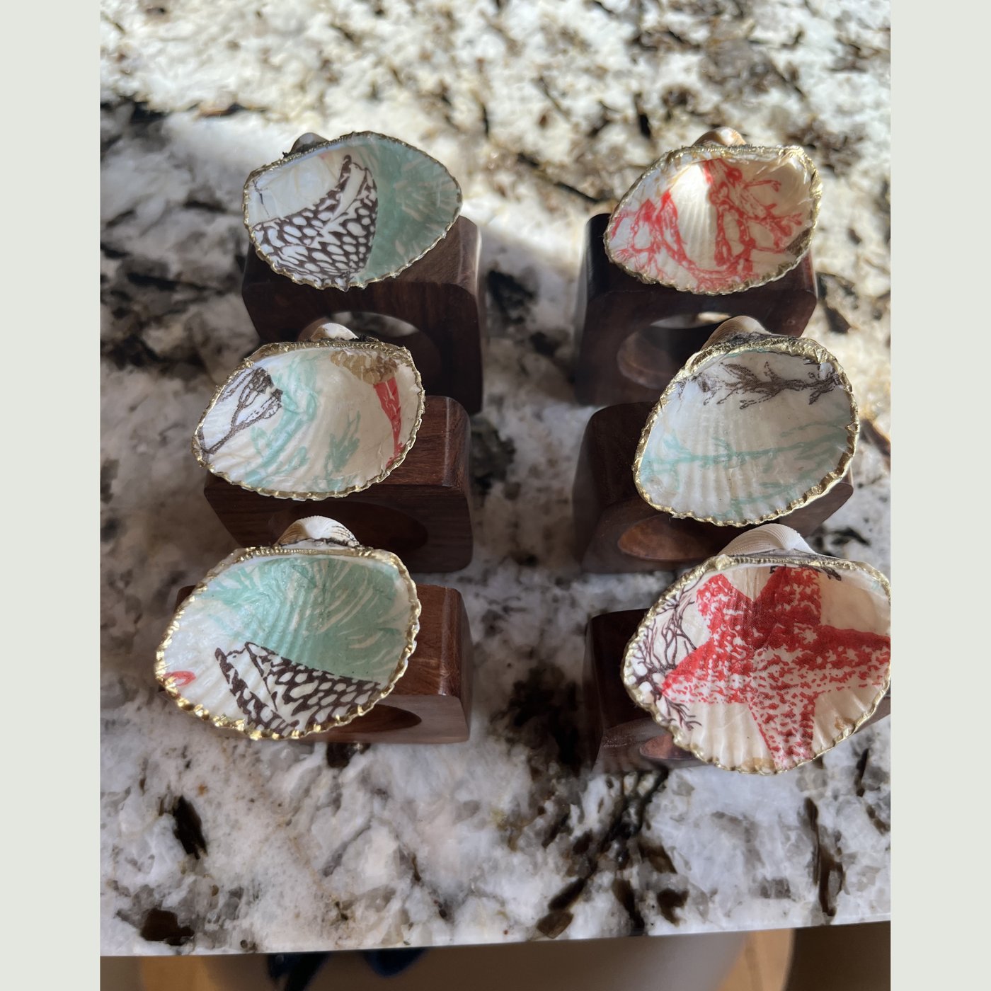 Gold-rimmed shell napkin rings alternating teal and coral patterns.