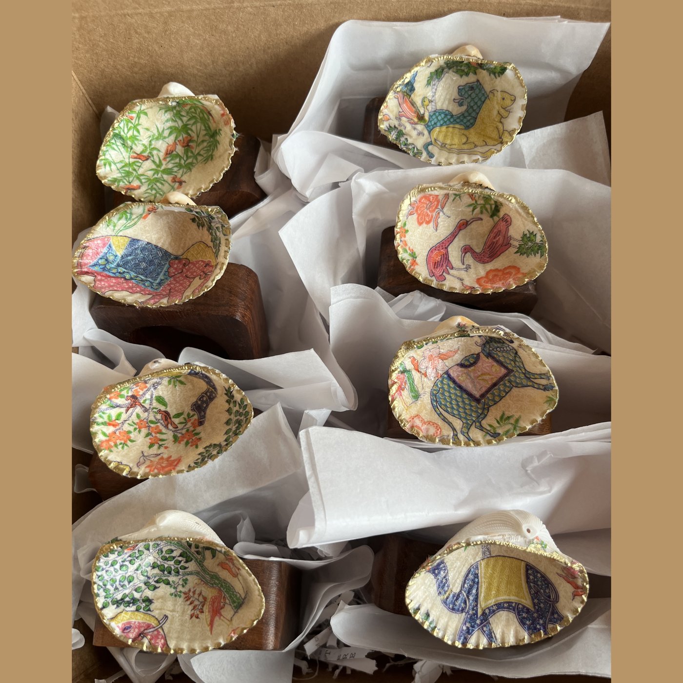 Gold-rimmed shell napkin rings, each featuring a different chinoiserie scene or animal.