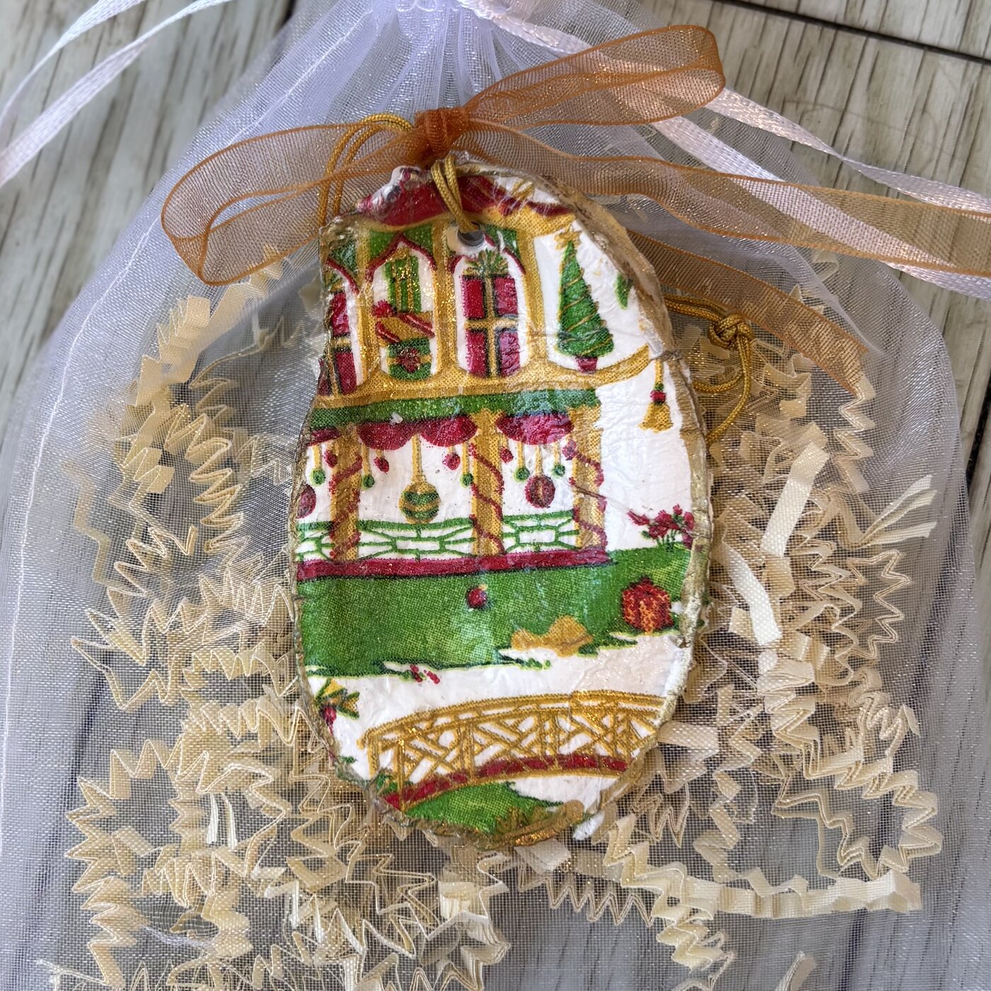 A gold-rimmed oyster shell ornament with a festive chinoiserie-style Christmas house. Comes in a gift bag.