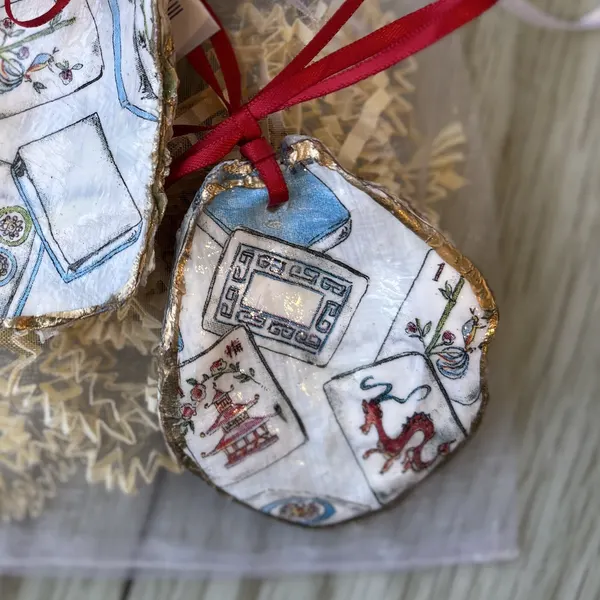 An oyster shell ornament covered in mahjong tiles. Each one shows a different mix of tiles. Comes in a gift bag.