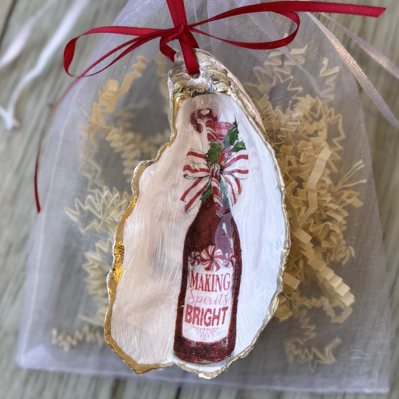 A gold-rimmed oyster shell ornament with a peppermint-bowed "Making Spirits Bright" bottle. Comes in a gift bag.