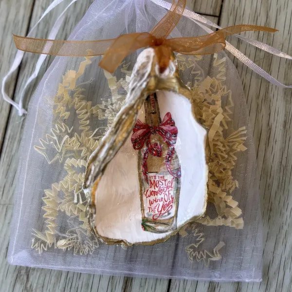 A gold-rimmed oyster shell ornament with a plaid-bowed "It's the Most Wonderful Wine of the Year" bottle. Comes in a gift bag.