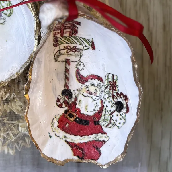 A gold-rimmed oyster shell ornament with a vintage Santa carrying a stack of presents. Comes in a gift bag.