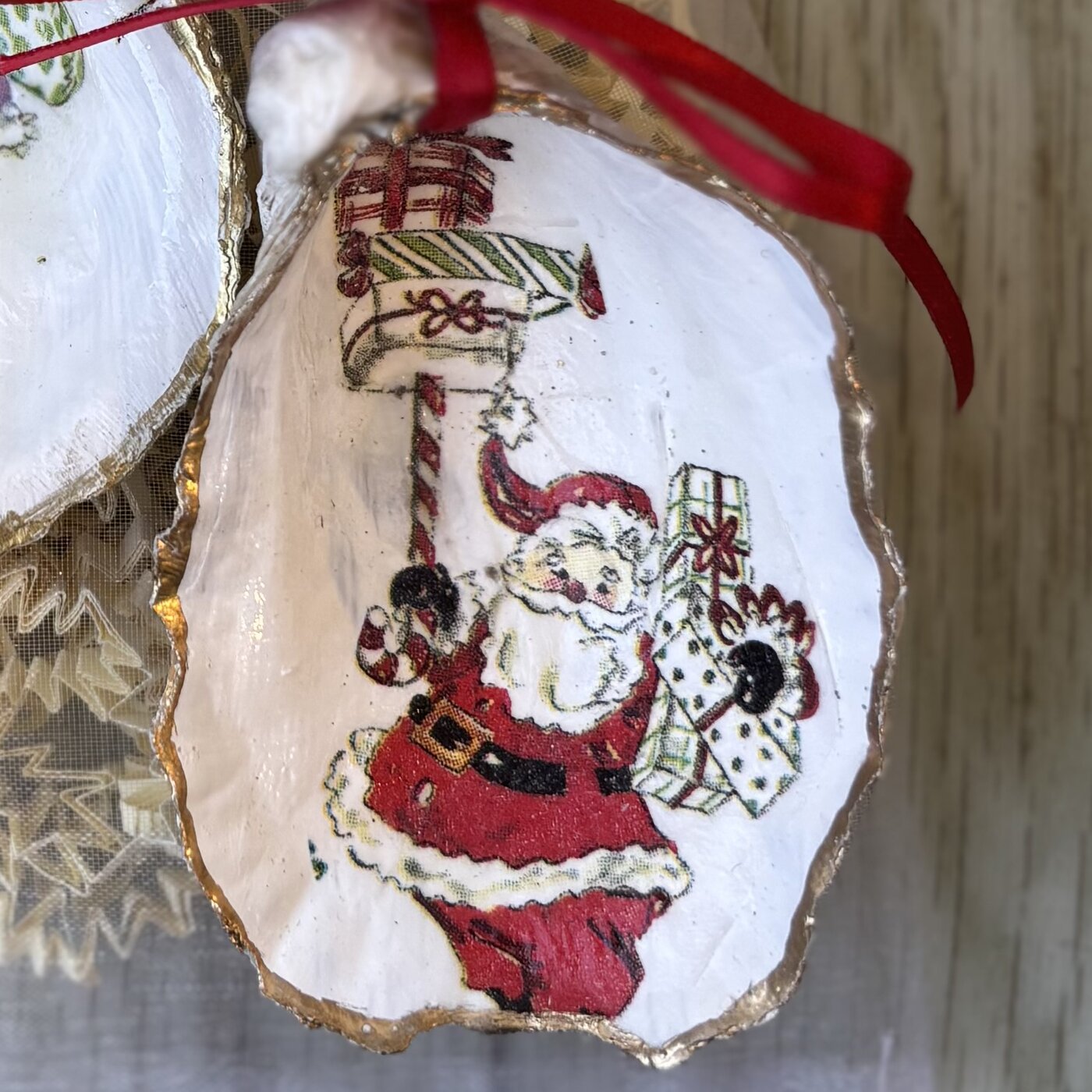 A gold-rimmed oyster shell ornament with a vintage Santa carrying a stack of presents. Comes in a gift bag.