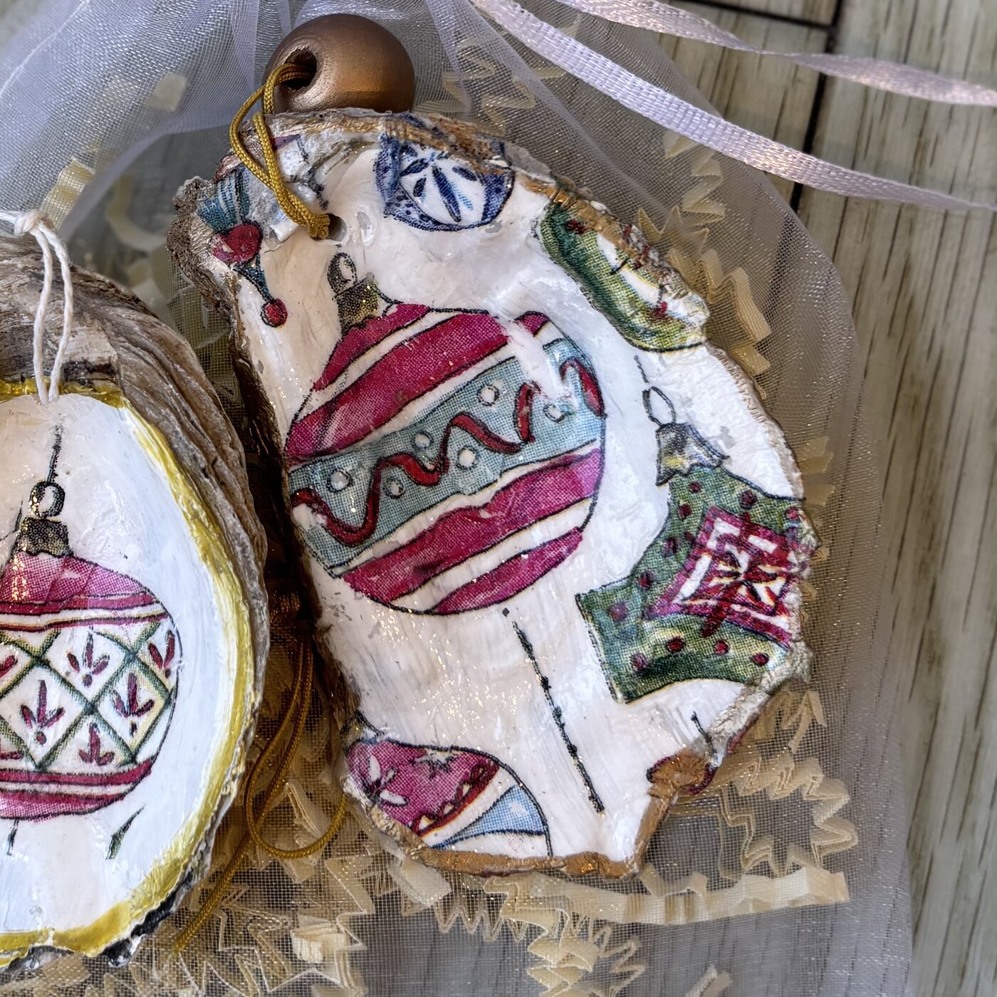 An oyster shell ornament covered in vintage Christmas baubles, finished with a wood bead. Comes in a gift bag.