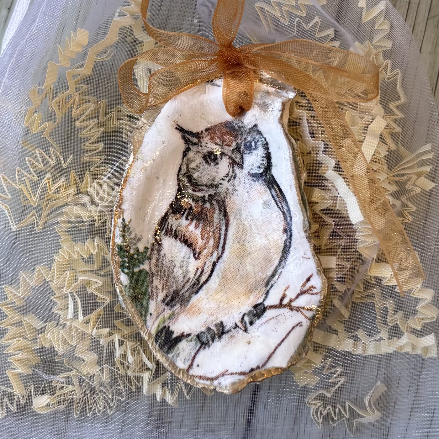 A gold-rimmed oyster shell ornament with an owl perched on a winter branch. Comes in a gift bag.