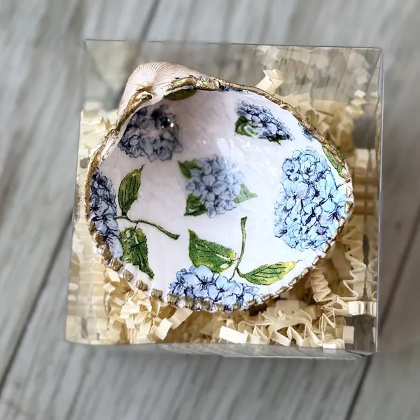 A gold-rimmed shell ring dish scattered with blue hydrangea blooms. Comes in a gift box.
