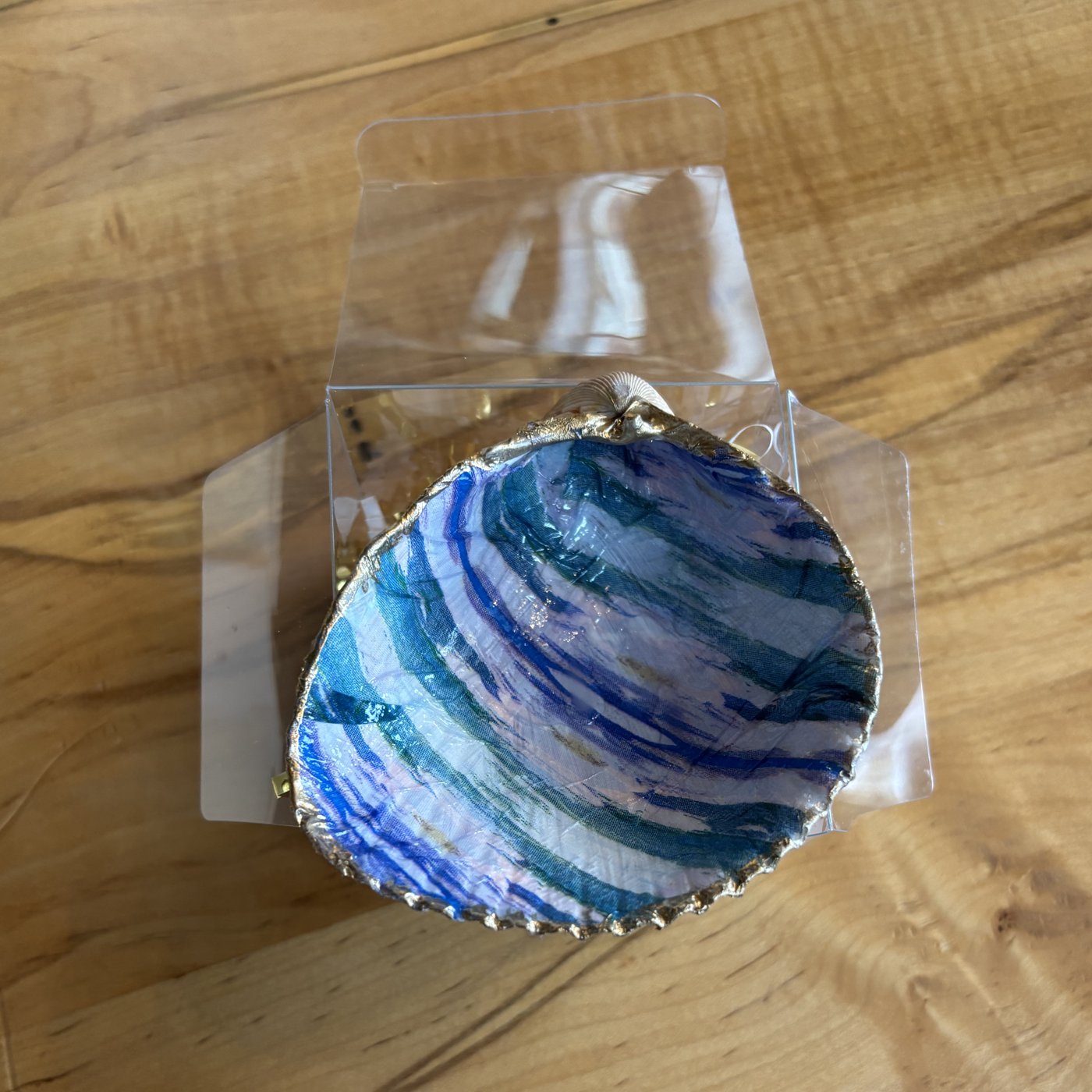 A gold-rimmed shell ring dish with a blue, teal, and purple swirl design. Comes in a gift box.