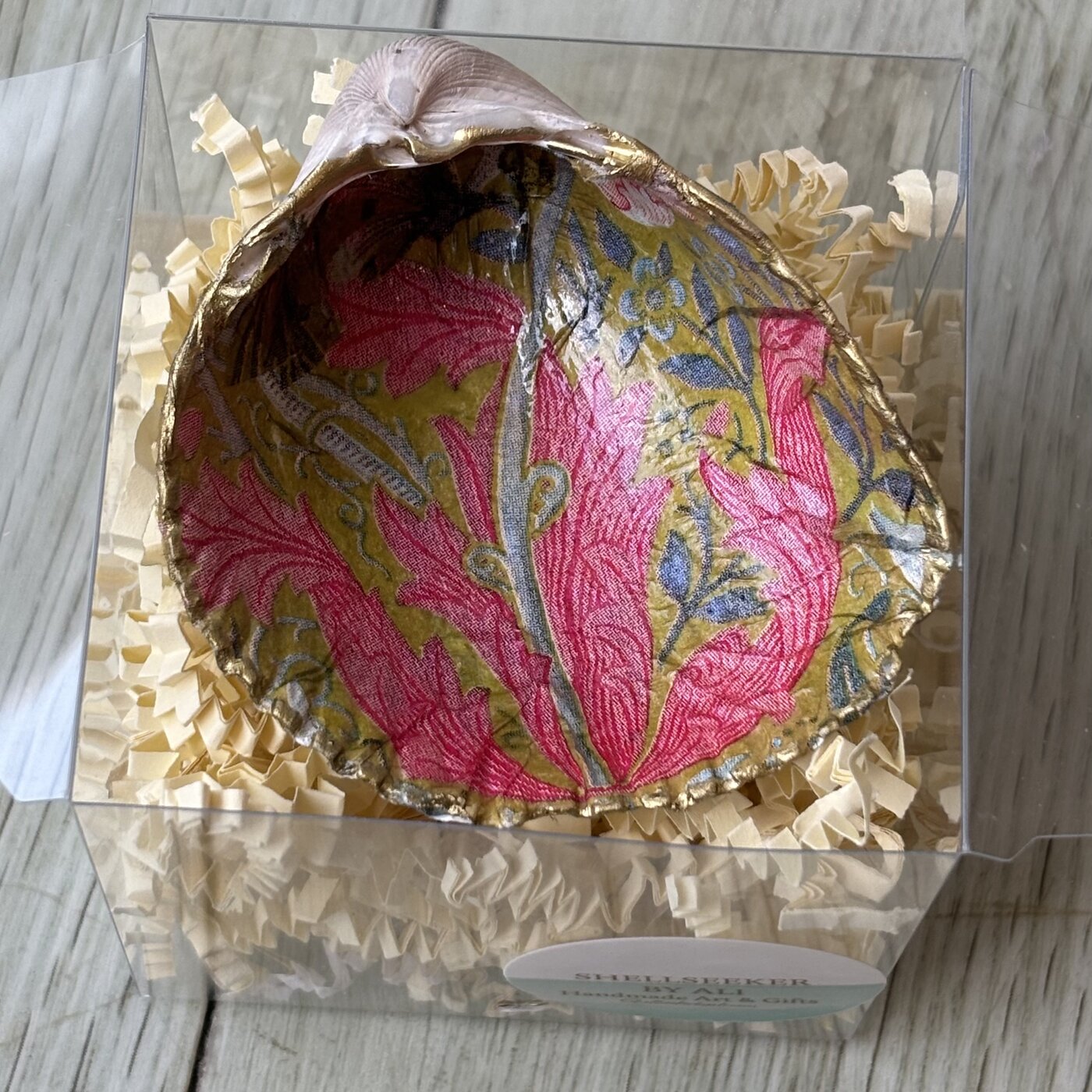 A gold-rimmed shell ring dish in a pink coral and olive leaf pattern. Comes in a gift box.
