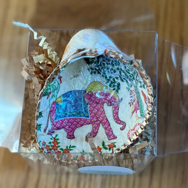 A gold-rimmed shell ring dish with a pink elephant in a blue saddle blanket among garden flowers. Comes in a gift box.