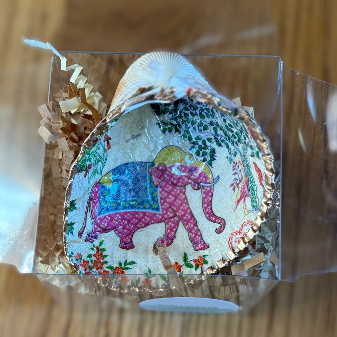 A gold-rimmed shell ring dish with a pink elephant in a blue saddle blanket among garden flowers. Comes in a gift box.