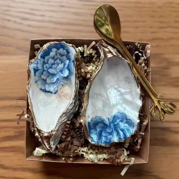 A pair of gold-rimmed oyster shell cellars with blue and white peonies on pearly white, with two gold or wooden spoons. Comes in a gift box.