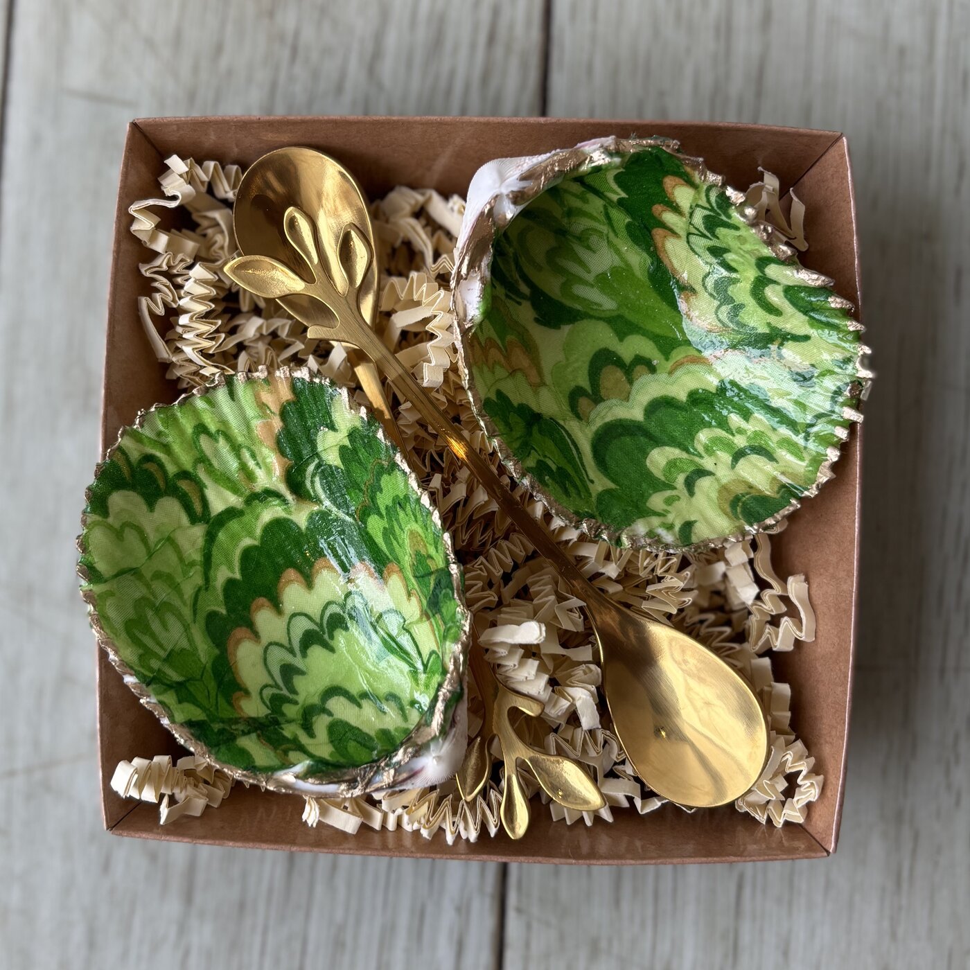 A pair of shell cellars in a swirled green marbled pattern, gold-rimmed, with two gold or wooden spoons. Comes in a gift box.
