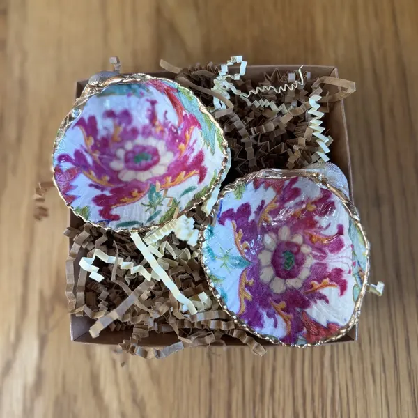 A pair of gold-rimmed shell cellars with a bold magenta tobacco leaf pattern on white, with two gold or wooden spoons. Comes in a gift box.