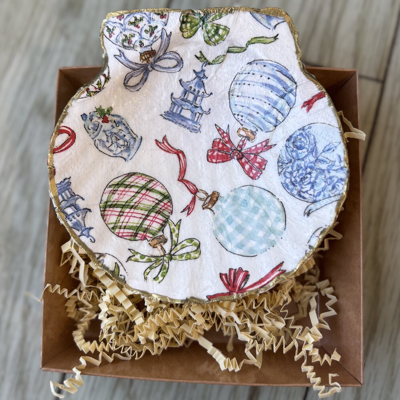 A gold-rimmed scallop shell dish covered in blue and white chinoiserie ornaments, plaid baubles and red bows. Comes in a gift box.