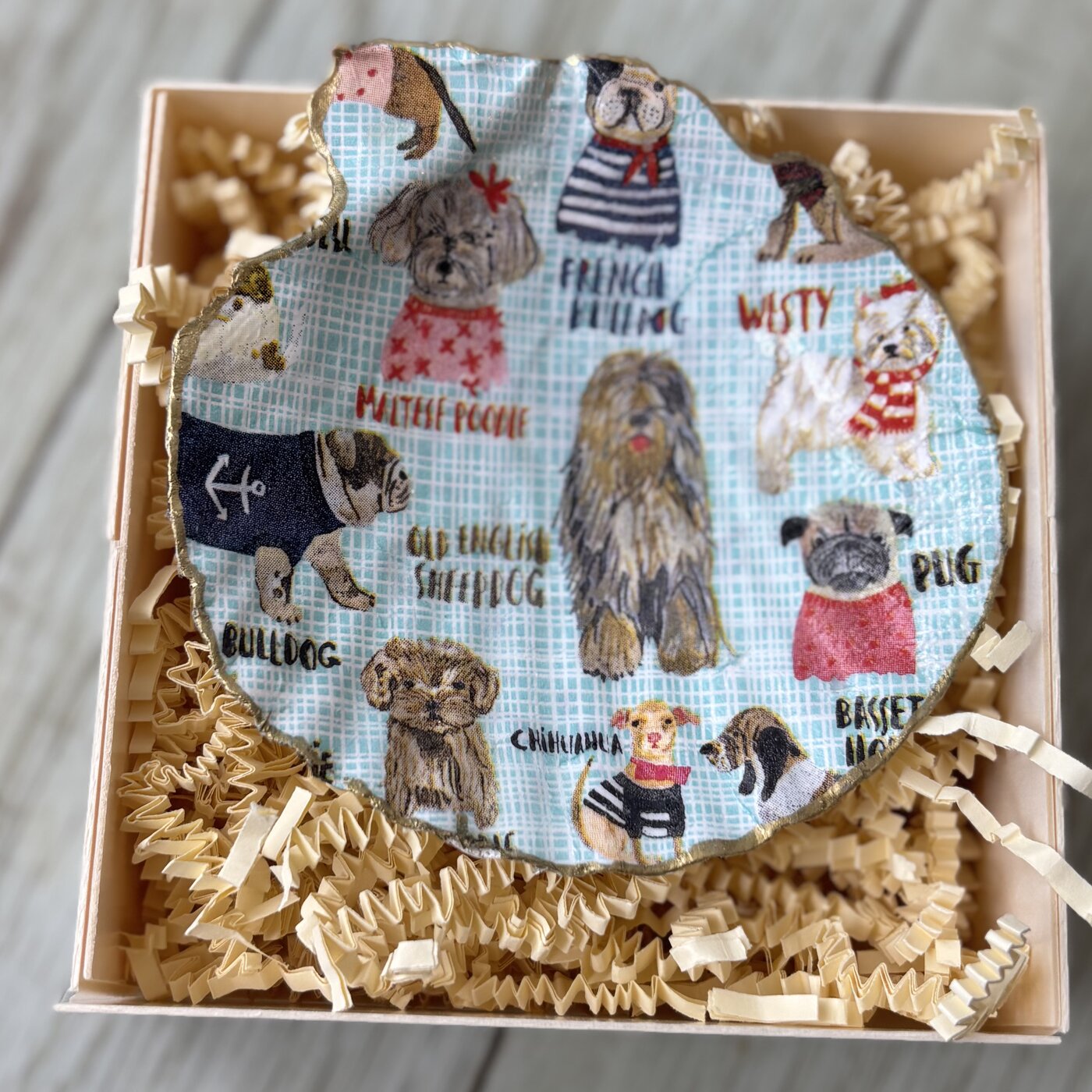 A gold-rimmed shell dish covered in illustrated dog breeds. Comes in a gift box.