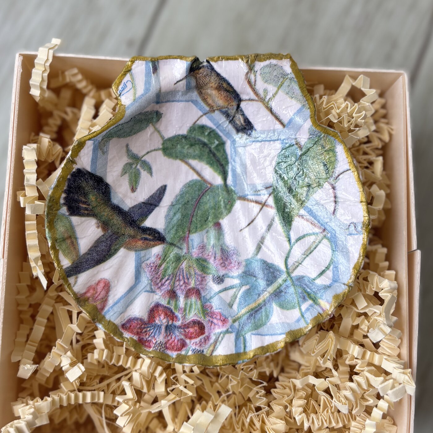 A gold-rimmed shell dish with hummingbirds among trailing blossoms. Comes in a gift box.