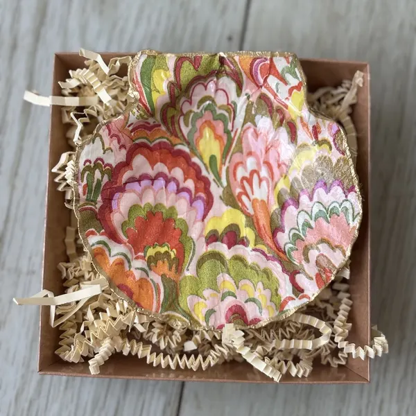 A gold-rimmed shell dish in a marbled scallop pattern of coral, pink and gold. Comes in a gift box.