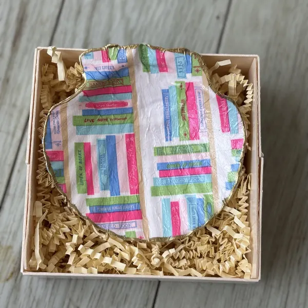 A gold-rimmed shell dish patterned with stacks of pastel books. Comes in a gift box.