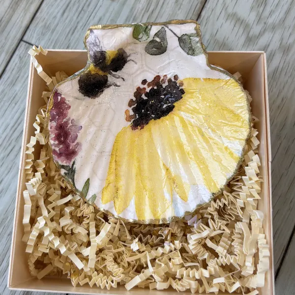 A gold-rimmed scallop shell dish with a sunflower, lavender and a bumblebee. Comes in a gift box.