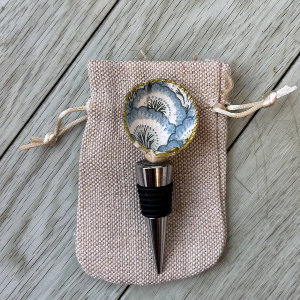 A wine bottle stopper topped with a shell in a blue and white fan pattern.