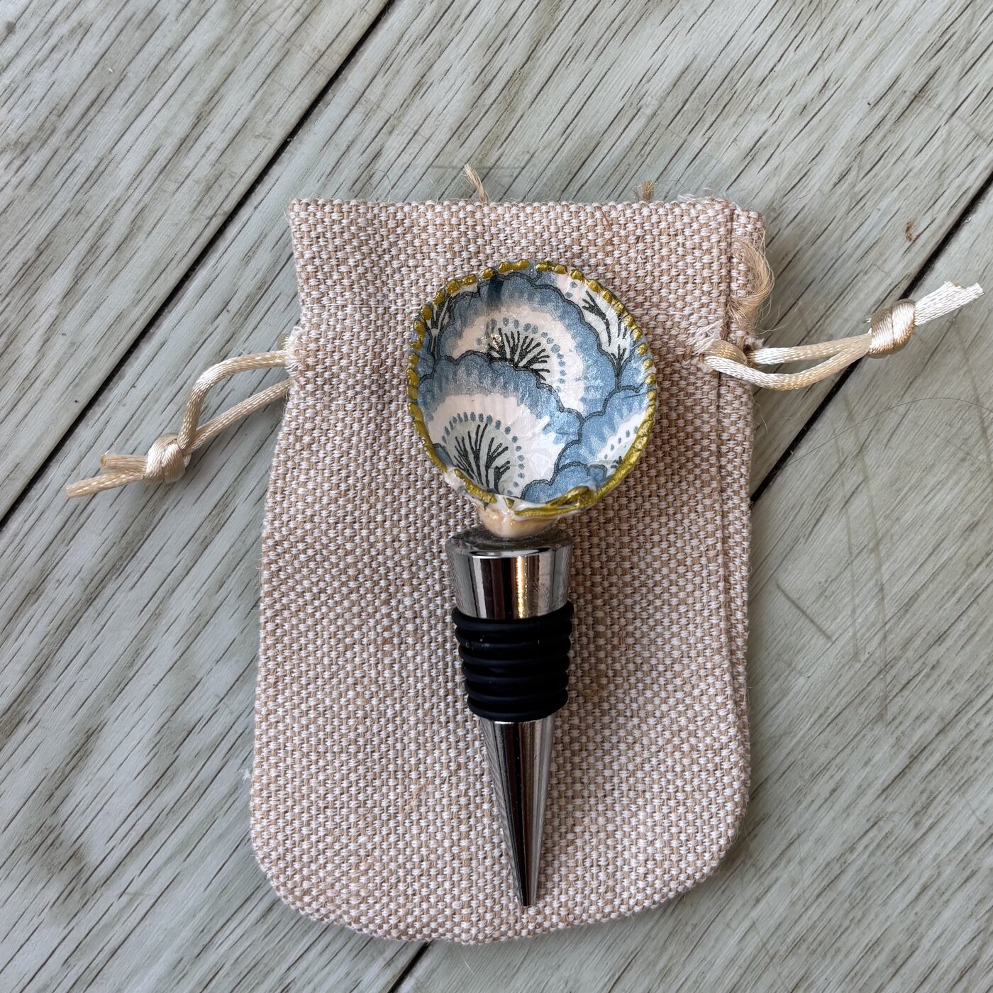 A wine bottle stopper topped with a shell in a blue and white fan pattern.
