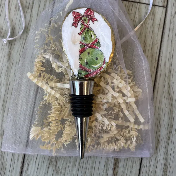 A wine bottle stopper topped with a gold-rimmed shell showing a ribbon-wrapped Christmas tree. Comes in a gift bag.