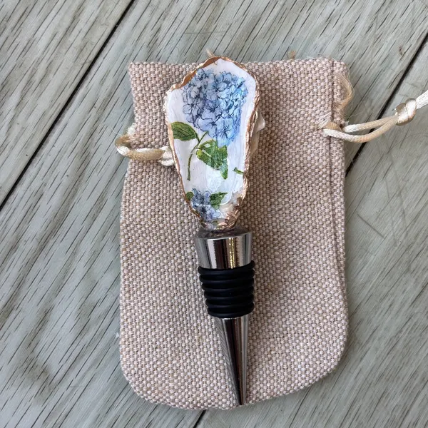 A wine bottle stopper topped with an oyster shell in blue hydrangea blooms.