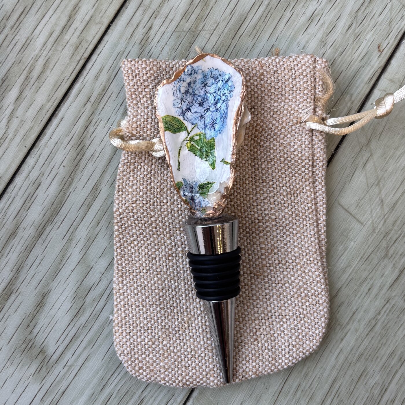 A wine bottle stopper topped with an oyster shell in blue hydrangea blooms.