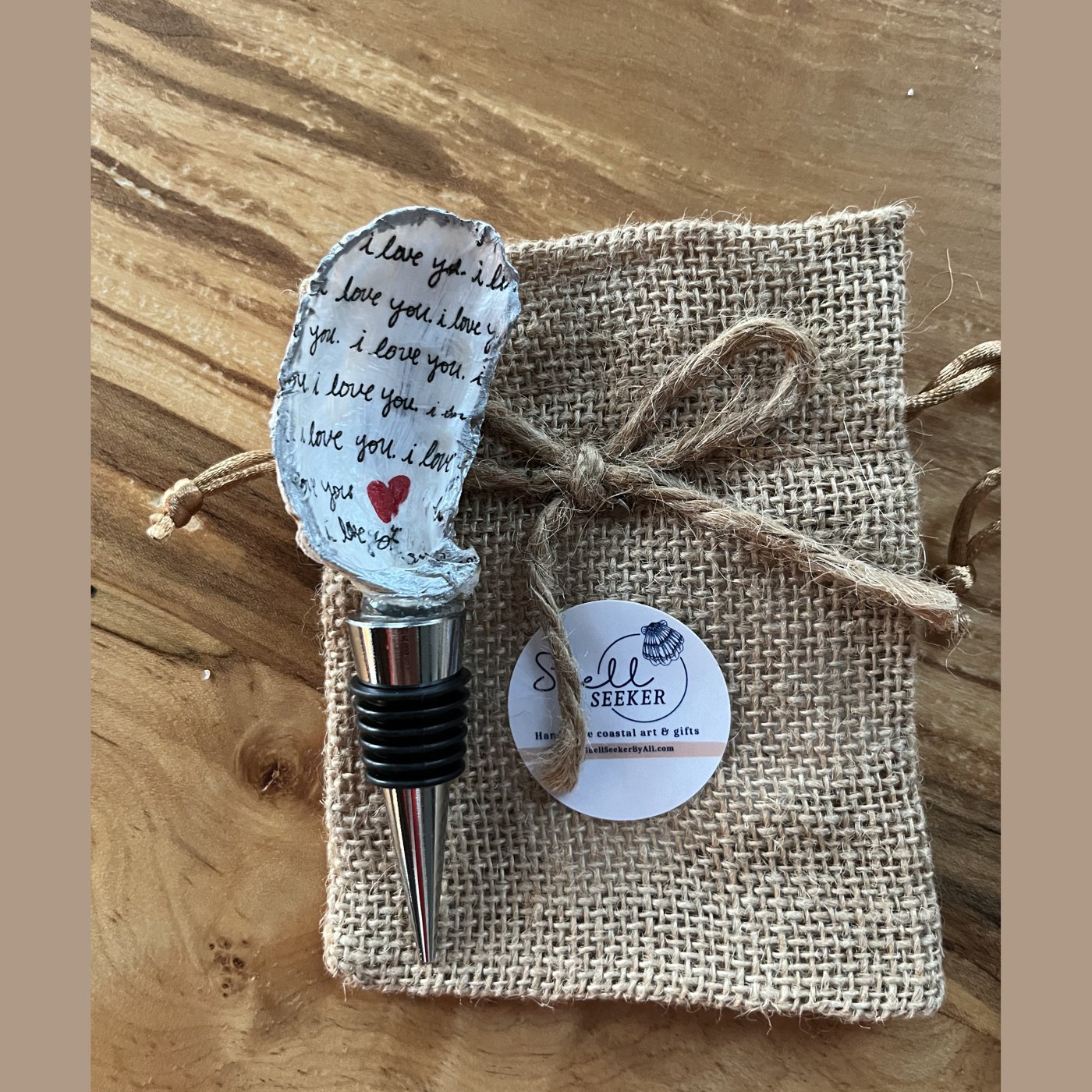 A wine bottle stopper topped with a shell hand-lettered in a repeating "I love you" script.