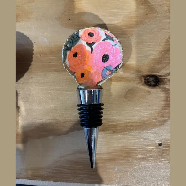 A wine bottle stopper topped with a shell in a bright pink and orange floral pattern.