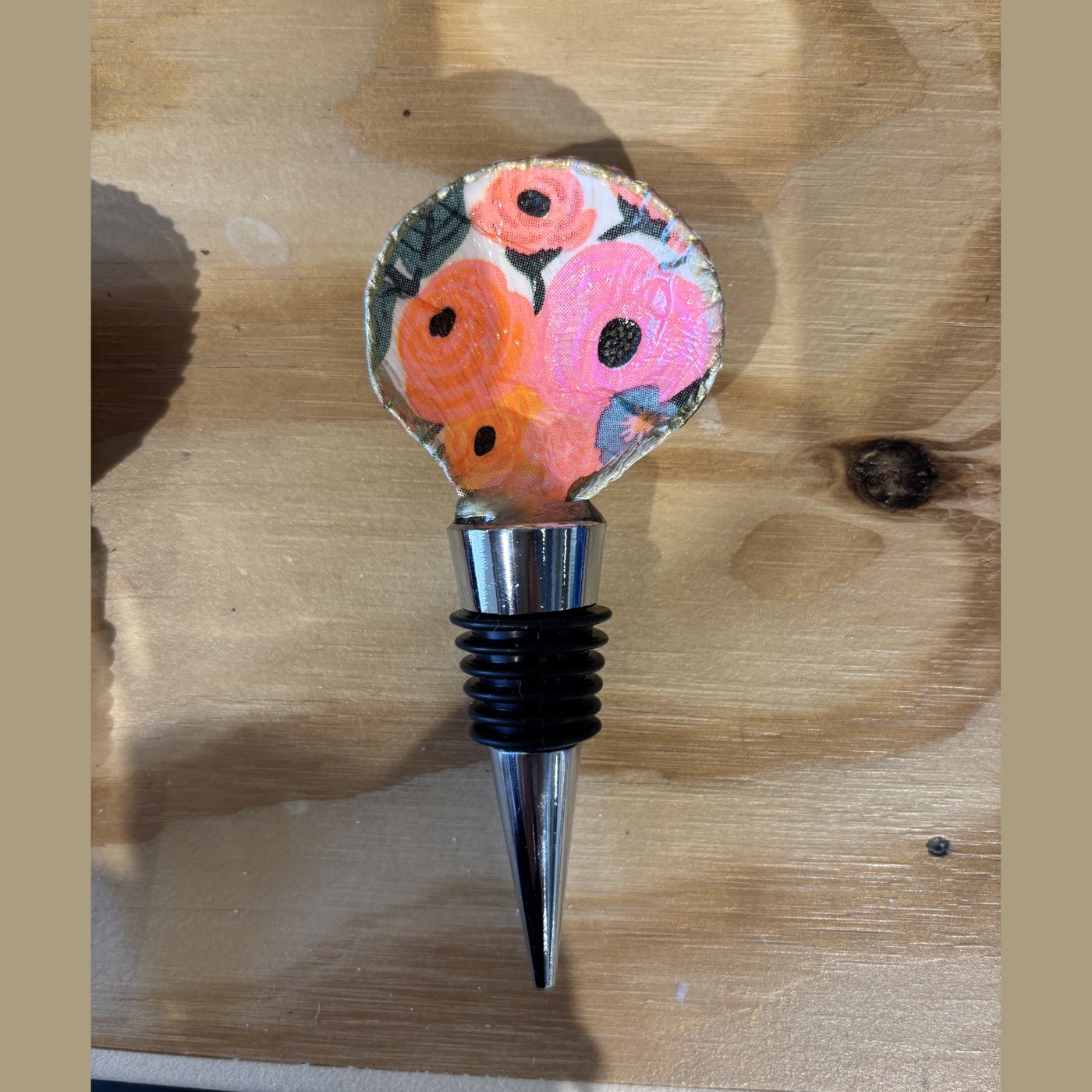 A wine bottle stopper topped with a shell in a bright pink and orange floral pattern.